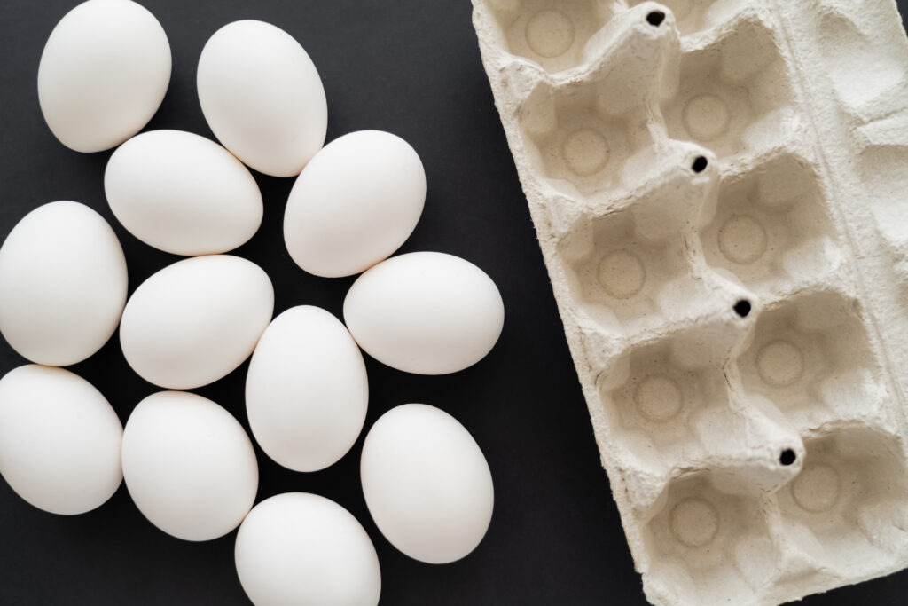 top view of carton tray and white eggs on black background