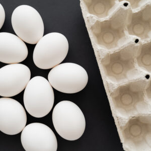 top view of carton tray and white eggs on black background